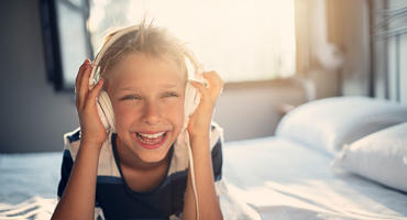 Junge liegt auf einem Bett und hört Musik über Kinderkopfhörer