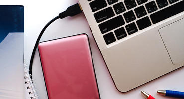 Arbeitsbereich mit Büchern, Stiften und einer rosa externen Festplatte, die an einen Laptop-Computer angeschlossen wird