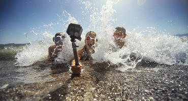 Kinder spielen in Meereswellen und filmen sich mit wasserdichter Action-Kamera.