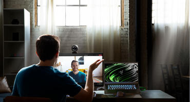 Razer Kiyo Pro Webcam auf einem Bildschirm montiert. Davor sitzt ein Mann und spricht mit einer Person auf dem Bildschirm per Videochat.