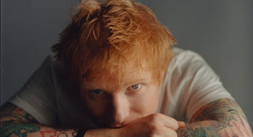 Ed Sheeran, Kinn aufgestützt auf die Unterarme, blickt in die Kamera