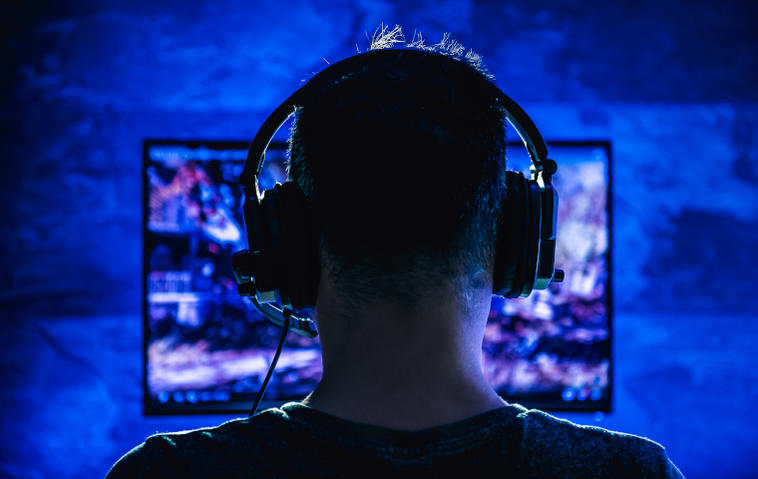 Hinterkopf eines Mannes, der ein Headset trägt und im dunklen Raum am Fernseher spielt.