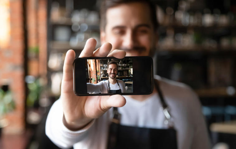 Mann hält kleines Smartphone für Selfie lächelnd vor sich